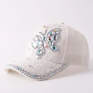 Vista detallada de la elegante gorra de encaje blanco con brillante mariposa de pedrería.