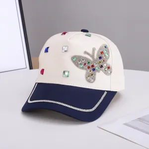 Vista detallada de gorra de béisbol beige y azul con mariposa de diamantes de imitación y cristales.