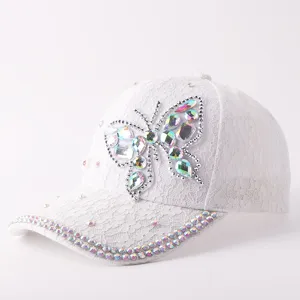 Detalle de la gorra de encaje blanco con brillante mariposa de pedrería irisada y elegante.