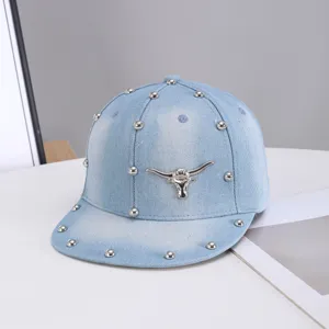 Vista detallada de gorra de béisbol de mezclilla azul claro con calavera de toro y remaches.