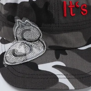 Vue détaillée d'un chapeau plat camouflage militaire avec patch strass et texte brodé.