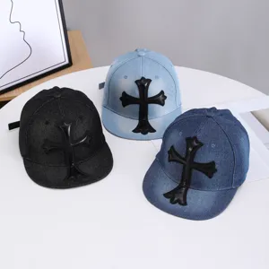 Vista detallada de gorras de béisbol de mezclilla con visera plana y parches de cruz de cuero negro.