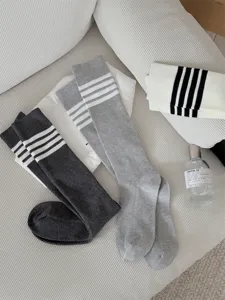 Grey ribbed knee high socks with white stripe details styled on white textured fabric surface.