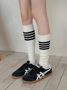 Close-up of white calf socks with black stripes worn with sneakers on wooden floor.
