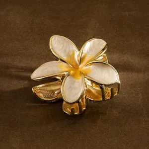 Close-up detail of a golden frangipani hair claw clip with white enamel petals.