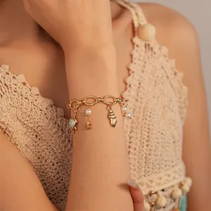 Close-up of ocean-themed gold charm bracelet with pearl and sea life pendants on wrist