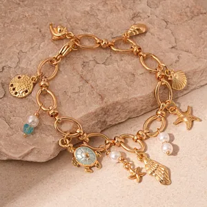 Close-up of gold ocean-themed charm bracelet with turtle, pearls and starfish on stone background.