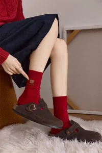 Nahaufnahme von gemütlichen roten Stricksocken mit süßer Bärenstickerei und braunen Clogs.