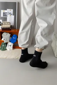 Detail view of men's black mid-calf socks featuring white embroidered letter GOD and cozy combed cotton.
