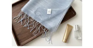 Light blue mulberry silk scarf with delicate fringes displayed on tray with cosmetic props.