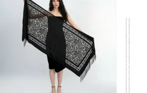 Dettaglio scialle in jacquard di velluto nero con motivi floreali eleganti e frange.