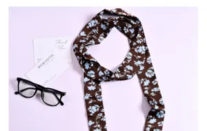 Dettaglio foulard twilly in seta con stampa floreale marrone e blu, nastro da collo.
