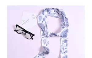 Primo piano di un foulard twilly con stampa paisley blu e bianca, perfetto per borse o capelli.