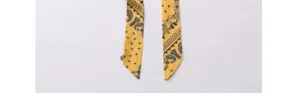 Primo piano della sciarpa twilly in seta gialla con classica stampa paisley nera e punte.