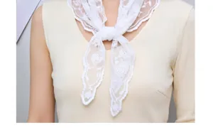 Vista detallada de un pañuelo triangular de encaje blanco bordado, diseño calado, elegante.