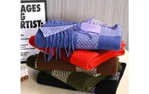 Detailed close-up of stacked winter plaid scarves featuring soft fringe and warm cashmere shawls.