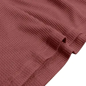 Close-up detail of men's waffle knit long sleeve fabric texture in dark pink red color.