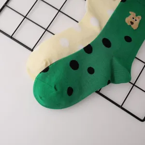 Primo piano dettagliato di calzini a pois verdi e crema con una simpatica toppa di orsetto.