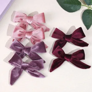 Detailed macro shot of six soft velvet bow hair clips in pink, purple, and burgundy