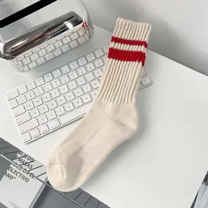 Detailansicht cremefarbene Sportsocken mit roten Streifen auf weißem Tisch.
