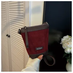 Detail shot of a wine red suede crossbody phone bag with dark brown leather trim and metal zipper.