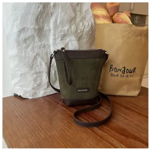 Detailed view of the dark green suede crossbody bag featuring brown leather trim and strap.
