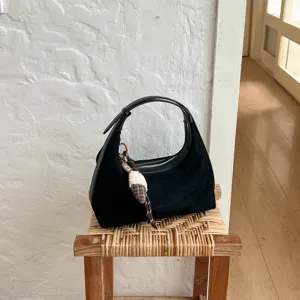 Detailopname van zwarte suède schoudertas met leuke hanger voor dagelijks gebruik.
