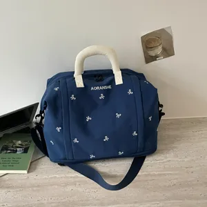 Vista detallada de la bolsa de viaje azul con bonitos bordados de lazo y asas de color crema.