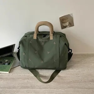 Vista detallada de la bolsa de viaje verde con bordado de lazo y asas resistentes.