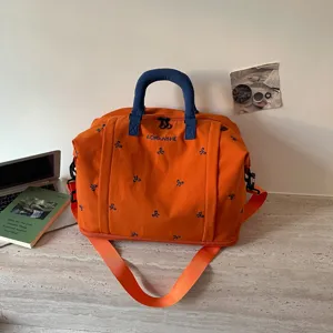 Bolsa de viaje deportiva de lona naranja con asas azules y bordado de lazos para viajes cortos.