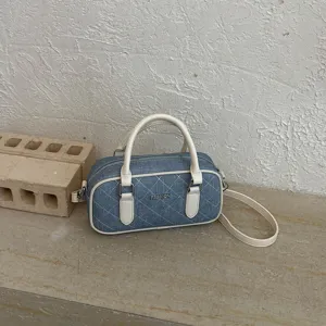 Detailansicht der Jeans-Kissen-Tasche mit Steppmuster, weißem Leder und Metallgriff.