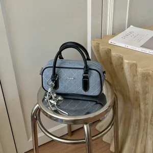 Nahaufnahme der blauen Jeans-Kissentasche mit schwarzen Ledergriffen und schicken Metallanhängern.