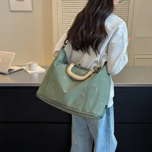 Vista detallada de la gran bolsa de viaje verde con bonito bordado de lazo y asa resistente.