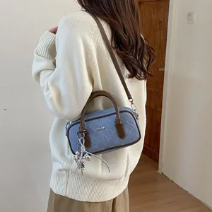 Detailansicht der stylischen Jeans Kissen Schultertasche mit braunem Besatz und Metallanhänger.