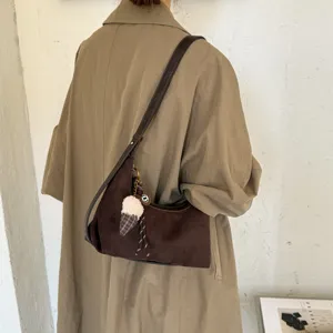Gedetailleerd aanzicht van een retro bruine suède schoudertas met pluche hangertje.