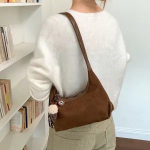 Detailopname van de bruine suède hobo schoudertas gedragen door model met gezellige trui.