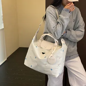 Detailopname van de grote casual tote bag met strikborduursel en stijlvolle driehoek plaat.