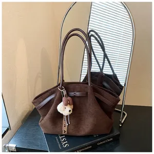 Detailed view of brown suede tote bag with double handles, side straps, and cute bear pendant.