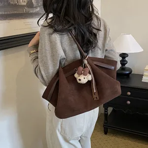 Detail view of brown suede tote bag with cute bear charm and pleated design in room setting.