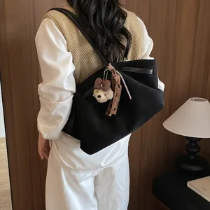 Detail view of black pleated shoulder tote bag with cute bear charm and patterned ribbon accent.