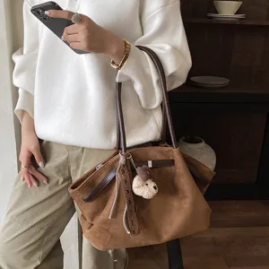 Brown suede shoulder tote bag detail view with plush bear pendant and ribbon decoration.