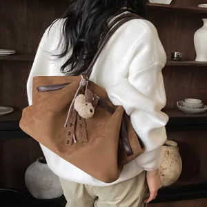 Detail shot of the brown suede shoulder bag showcasing its unique pleated design and plush bear charm.