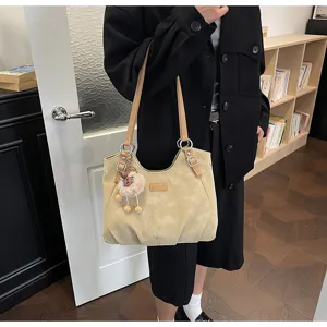 Primo piano di borsa a tracolla beige vintage con ciondolo in peluche per uso quotidiano.