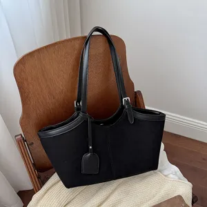 Detailed view of black suede women tote bag, minimalist shoulder handbag closeup in home setting.