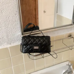 Λεπτομερές κοντινό πλάνο μαύρης καπιτονέ τσάντας ώμου με μεταλλική αλυσίδα και λαβή.