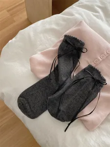 Dark grey mid-calf socks featuring black ribbon bows and ruffle cuffs, paired with pink knit top.