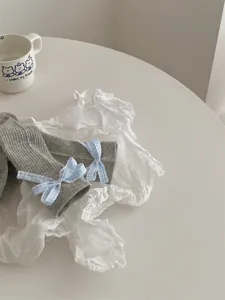 Detail shot of grey ribbed slouch socks featuring charming blue gingham bows, minimalist style.