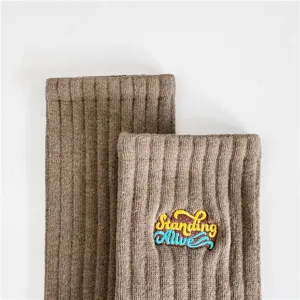 Gros plan de chaussettes montantes en coton côtelé kaki avec broderie colorée.