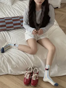 Cute cartoon black cat mid-tube socks detail view worn by model on bed, cozy style.