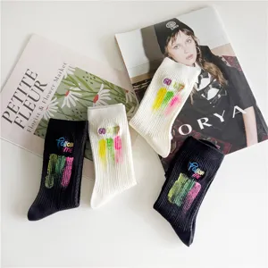 Vue détaillée de chaussettes mi-hautes noires et blanches avec lettres et éclaboussures brodées.